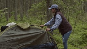 Long shot of young interethnic couple in hiking clothes pitching tent while camping in summer forest - Powered by Shutterstock - Get 15% off with code: PIKWIZARD15