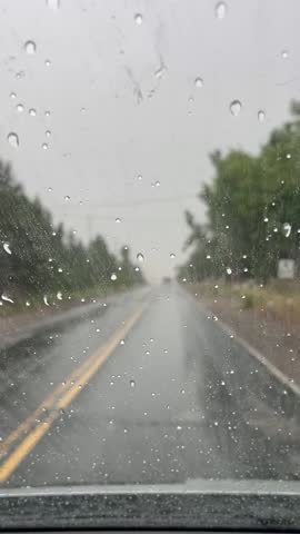 Raindrops on a car windshield during a drive on a grey, rainy day. The blurry road and distant car headlights create a moody, atmospheric feel, perfect for a cinematic or emotional scene.