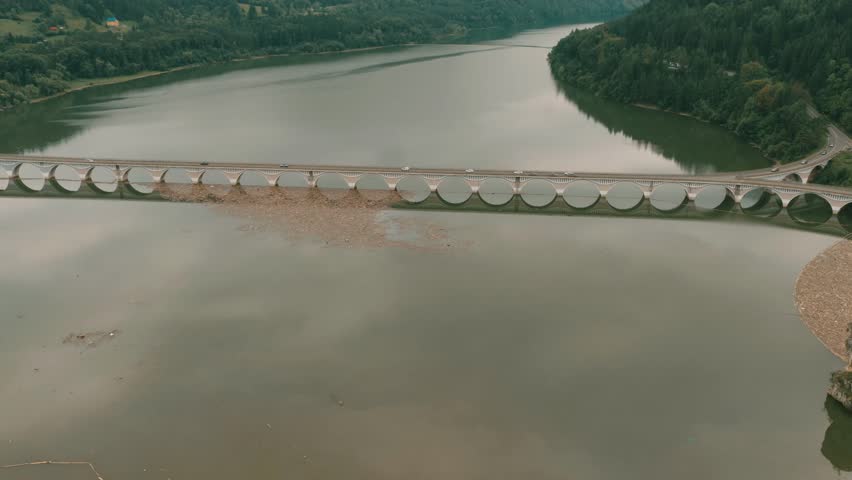 Logs and debris float on the surface of a flooded river in a mountain valley