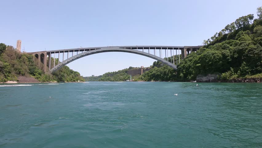SLOW MO - Niagara Falls International Rainbow Bridge, a steel arch bridge across the Niagara River, connecting the cities of Niagara Falls, New York, and Niagara Falls, Ontario, seen from a boat tour.