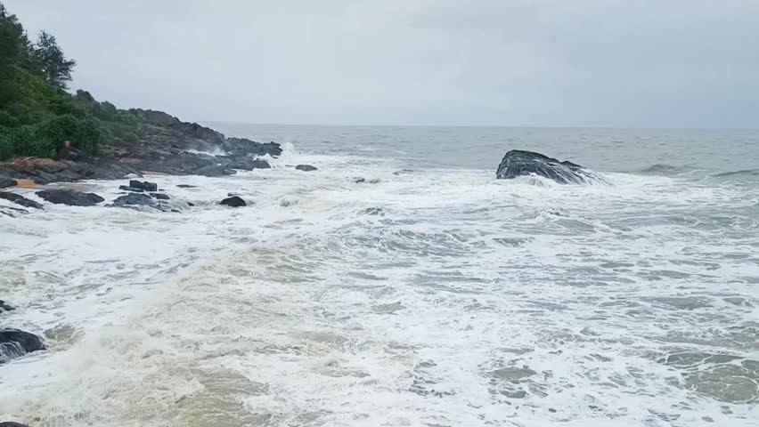 footage of ocean waves gently crashing against tetrapod rock barriers on a serene beach. Ideal for background, nature, travel, or environmental themes with calm sea and sandy shoreline.