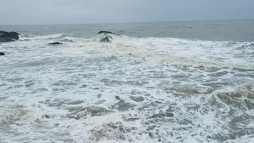 footage of ocean waves gently crashing against tetrapod rock barriers on a serene beach. Ideal for background, nature, travel, or environmental themes with calm sea and sandy shoreline.