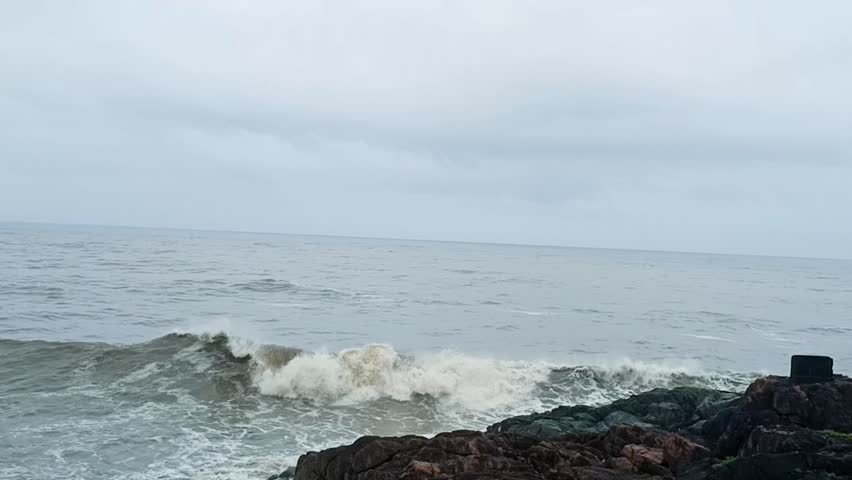 footage of ocean waves gently crashing against tetrapod rock barriers on a serene beach. Ideal for background, nature, travel, or environmental themes with calm sea and sandy shoreline.