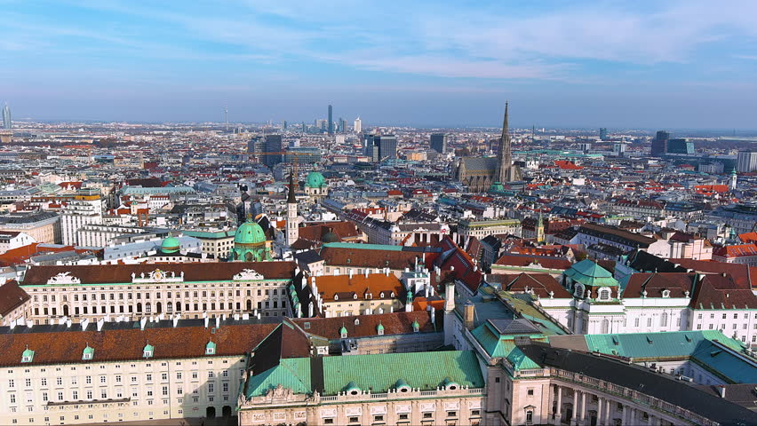 4K drone panorama over the Hofburg’s copper rooftops toward St. Stephen’s Cathedral and Vienna’s skyline - imperial domes, baroque facades and modern towers under a clear blue sky in Austria.