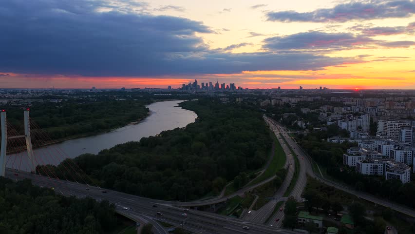 Cheap apartment blocks in suburb district of Warsaw city, Poland. Colored sunset evening in polish capital town. Cars crossing Vistula River on Siekirkowski bridge. Skyline of downtown in background.