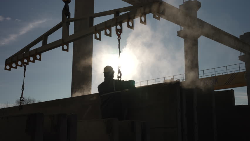This silhouette image of a worker lifting concrete with steam in the background symbolizes labor, dedication, and the transformation of raw materials into structures, fa01