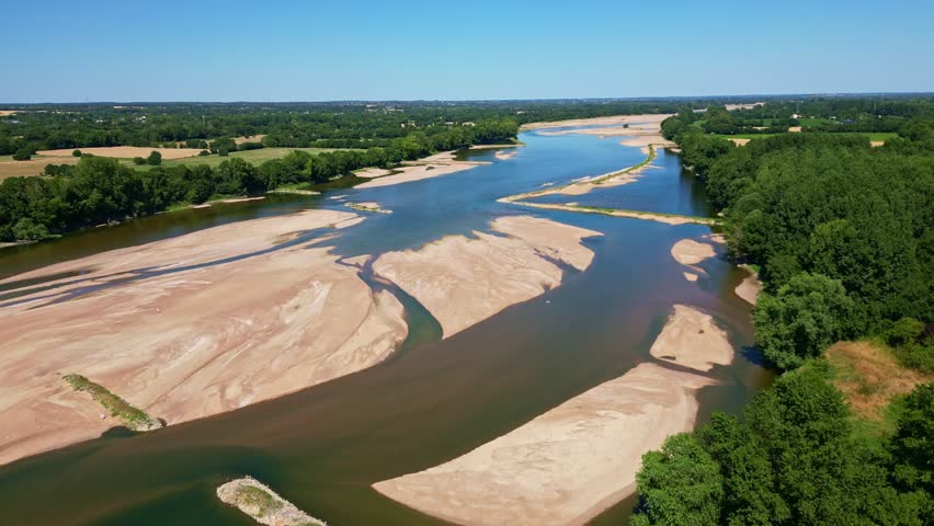 Loire River with sandbanks, green forest on riverbanks under clear blue sky, Loireauxence, France. Aerial drone forward