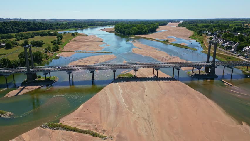 Drone pullback shot showing Varades suspension bridge over low Loire River with visible sandbanks and surrounding vegetation - Loireauxence in France