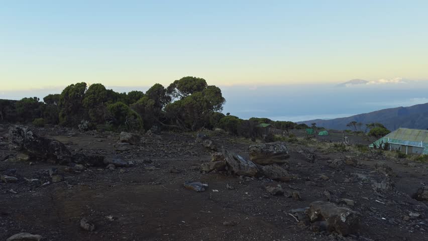 Open rocky plateau on Mount Kilimanjaro with soft sky and rugged volcanic terrain, establishing pan at campsite