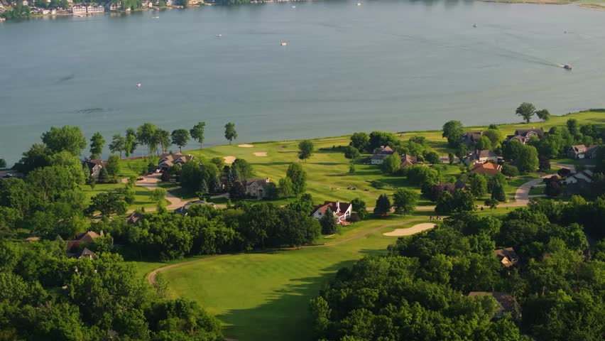 Aerial tilt down of golf course along Lake Como Wisconsin with green fields and trees along edge of calm reflective water