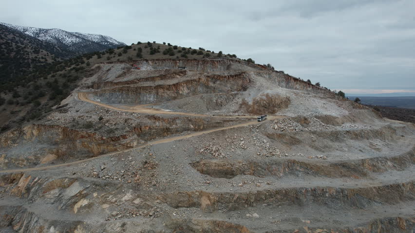 This aerial shot portrays the intricate network of mining roadways leading into the depths of a quarry, revealing layers of extracted materials and geological formations, fa01