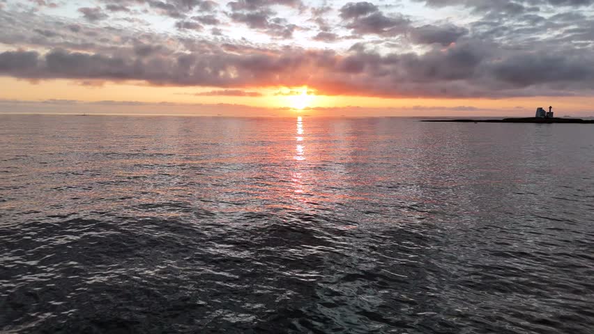 An Aerial view of sunlight reflecting in the surface of water as a drone flies towards the setting sun in ocean outside the island of Averoya, Norway