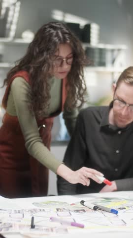 Close Up Team Of Creative Designers Are Looking At The Project Blueprint, Talking About Them, Sitting Together At The Table. Modern Informal Office. Friendly Working Atmosphere. Vertical Video