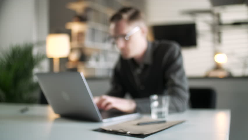 Professional Creative Man Sitting At His Desk In Home Office Studio Working Typing On a Laptop. Doing Research And Look At Camera. Glass Reflection. Busy Worker Freelancer Working On Notebook Device. - Powered by Shutterstock - Get 15% off with code: PIKWIZARD15