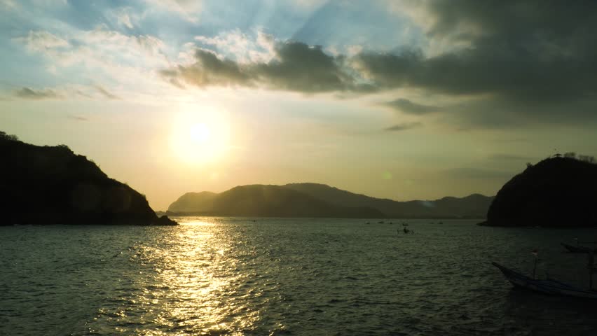 Sunset over ocean waves wash sand beach. Aerial sun set above mountain silhouette.