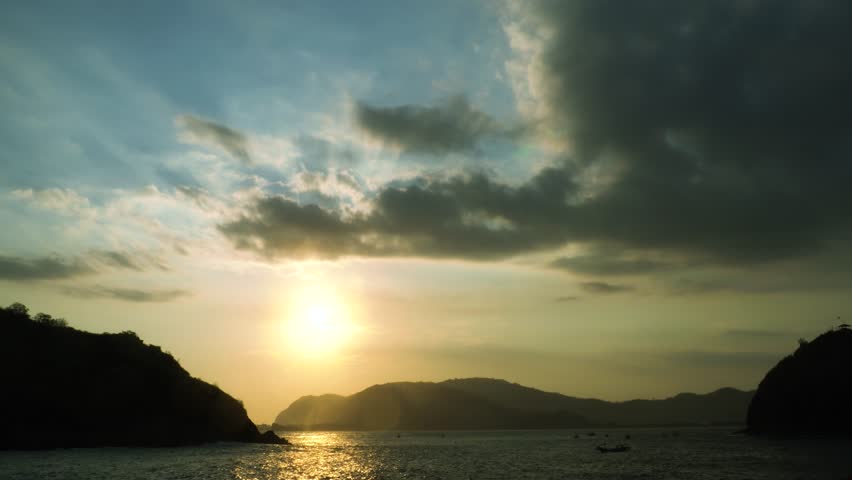 Sunset over ocean waves wash sand beach. Aerial sun set above mountain silhouette.
