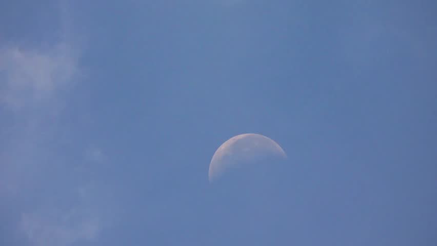 Half moon in the blue sky during daytime with some clouds around it