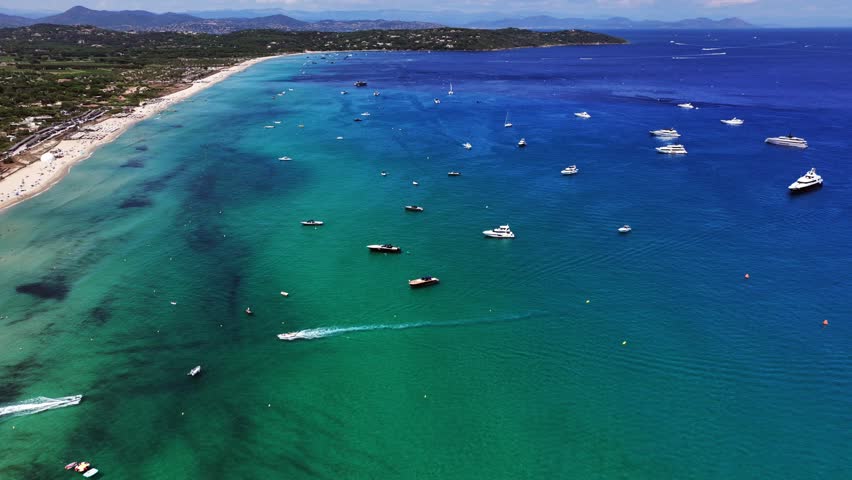 180° right pan from north part of Pampelonne Beach across the bay with many expensive luxury yachts anchored, to south part beach, green wooded hilly landscape in background - 4k video aerial footage