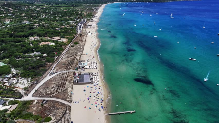 flying along famous Pampelonne Beach located at coastline of Ramatuelle, Côte d’Azur, France with people on the beach and in the water of Mediterranean Sea and many boats  - 4k aerial video footage