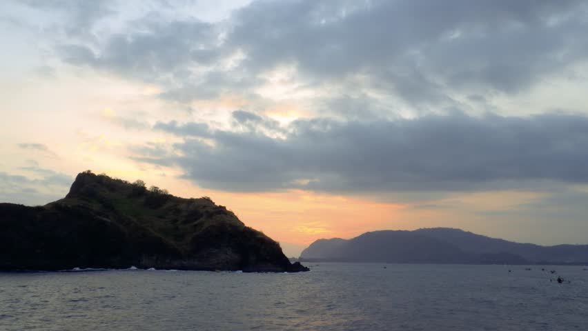Time lapse, Sunset over ocean waves wash sand beach. Aerial sun set above mountain silhouette