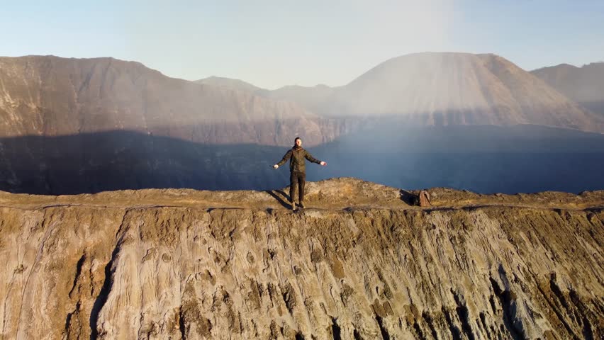 4K cinematic drone spiral orbit around a man raising arms on a volcano ridge. Rising and descending orbit captures freedom, scale, and dramatic volcanic scenery.