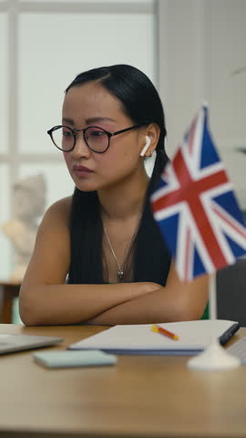 Young Korean woman taking British English course via laptop, writing in notebook