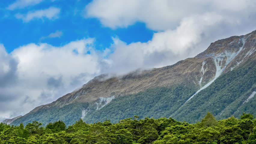 Distant green hill with forested slopes under a partly cloudy summer sky in the Christchurch region, viewed from afar in soft daylight.