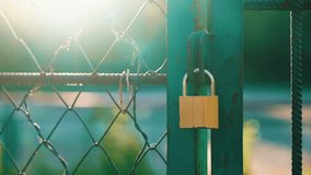 Metal gate with chain link fence locked with padlock at sports ground during golden hour sunset light - Powered by Shutterstock - Get 15% off with code: PIKWIZARD15