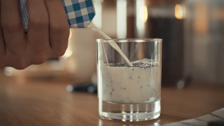 Large plan pours fresh milk into a transparent glass pouring chia seeds cooking healthy breakfast from natural chia seeds chiapuding. Healthy food healthy lifestyle