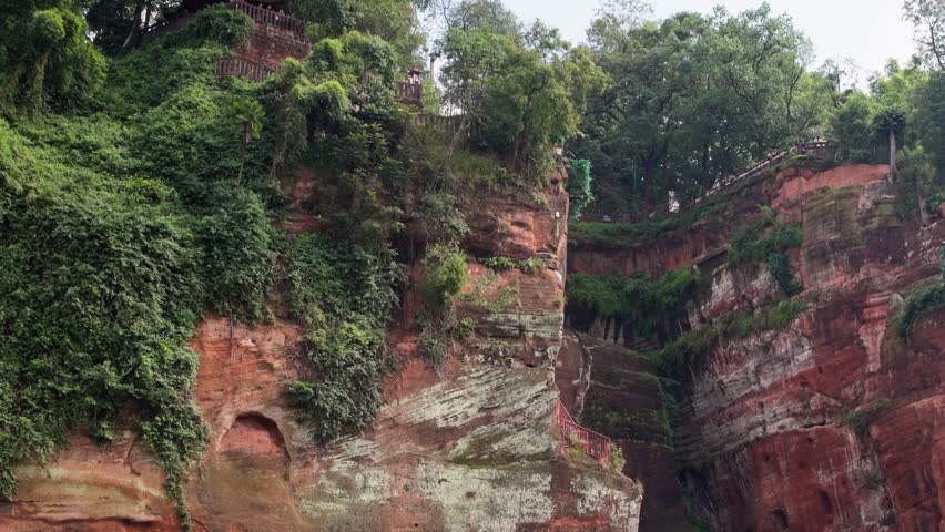 Wide slow motion shot of the entire Leshan Buddha from side angle, showing scale and surrounding natural context
