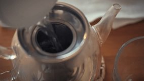 Hot water is being poured into a silver teapot that contains loose leaf tea. This takes place in a cozy kitchen setting, perfect for an afternoon tea experience - Powered by Shutterstock - Get 15% off with code: PIKWIZARD15