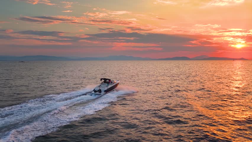 Aerial rear view of a motor speedboat cruising with speed over the ocean into the summer sunset
