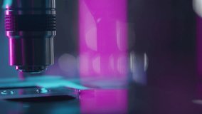 Microscope objective lens slowly moving above glass slide with liquid droplets in laboratory with colorful neon lighting and blurred bokeh background. Extreme close-up view - Powered by Shutterstock - Get 15% off with code: PIKWIZARD15