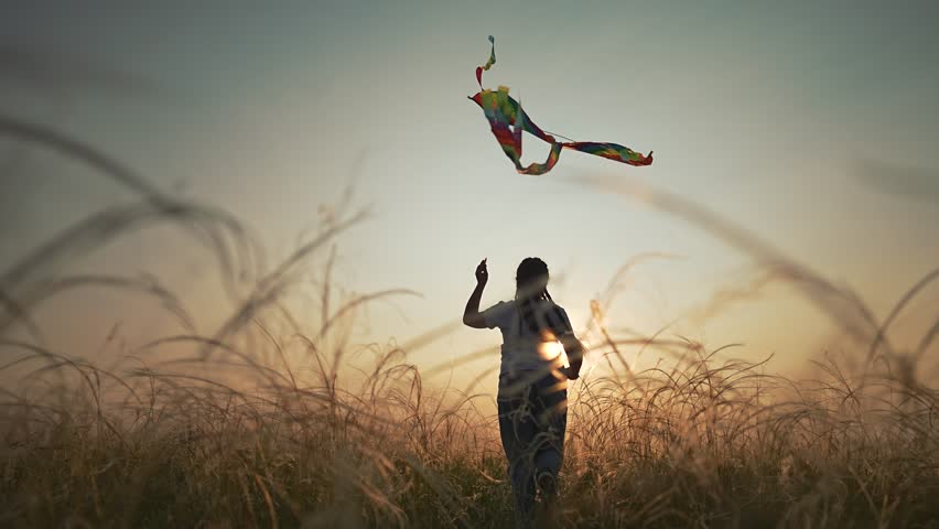 Kid holds kite string high in air while running through tall field. Outdoor summer freedom fills sky. Girl smiles flying kite, child enjoying peaceful sunset light, summer breeze, field, freedom, kid.