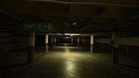 Dimly lit underground parking garage with concrete pillars and exit sign above center lane - Powered by Shutterstock - Get 15% off with code: PIKWIZARD15