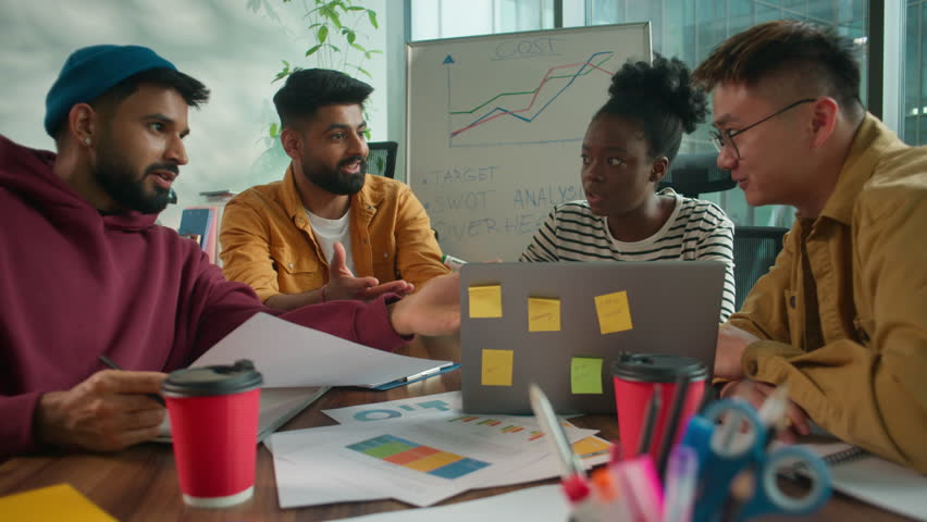 Informal business team four co-workers diversity people corporate group of multiracial workers discussing project strategy in coworking office pointing at laptop talking startup development teamwork