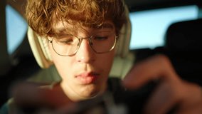 Close up of teenage boy with glasses wearing headphones and using smartphone in warm sunlight in the car - Powered by Shutterstock - Get 15% off with code: PIKWIZARD15