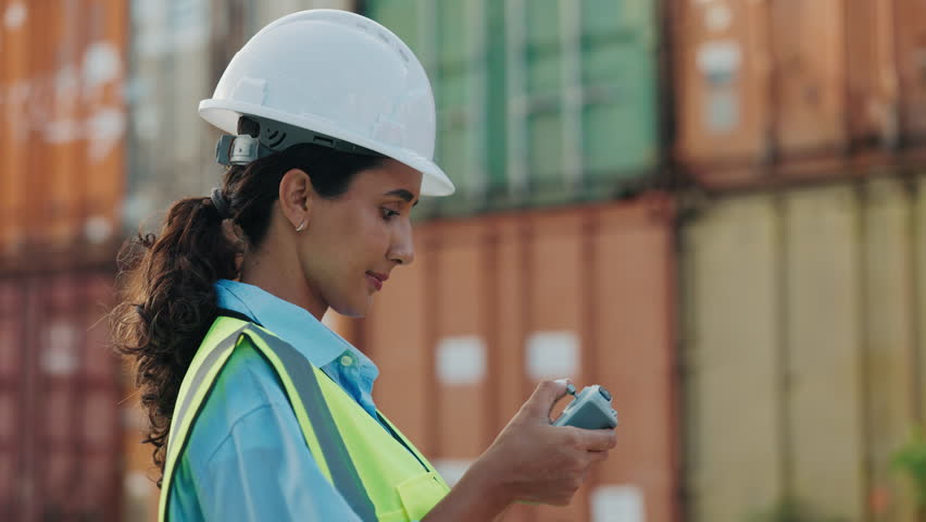 Forewoman Standing Outside near Warehouse Wearing White Helmet and Yellow Vest Operating Drone. Lady Engineer Working by Controlling Drone in Cargo Centre. Container Import And Logistics Concept