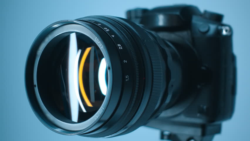 A professional camera on a tripod with an expensive lens with an aperture of 1.5 and a focal length of 85 mm, in which reflects the moving linear light. Closeup. Macro