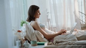 Relaxed freelancer working in bed typing laptop on white bedding. Serious woman browsing computer drinking coffee after wake up in home bed. Calm businesswoman reading email at weekend early morning. - Powered by Shutterstock - Get 15% off with code: PIKWIZARD15