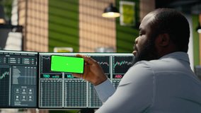 Prop firm worker in office learns new trading strategies from video lesson on green screen mobile phone. African american man using chroma key smartphone to watch educational content - Powered by Shutterstock - Get 15% off with code: PIKWIZARD15