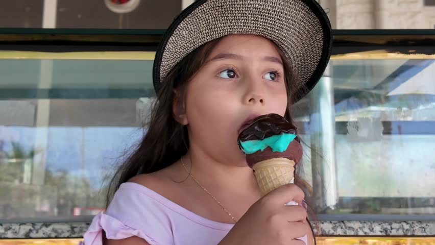 A 7-year-old girl is eating ice cream in a cone.