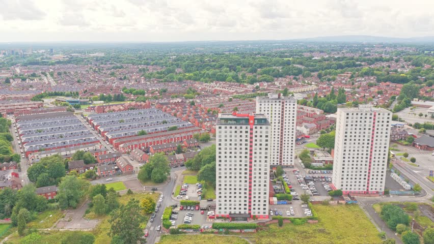 Salford city centre in Greater Manchester, England, shows high-rise residential blocks, rows of terraced houses, and green spaces stretching toward the distant horizon, captured in a static drone shot