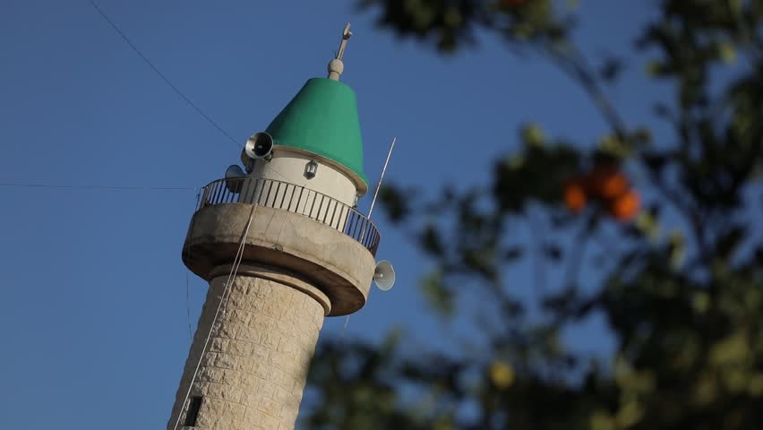 Close-up of mosque minaret with detailed stone structure and green dome, showcasing Islamic art, religion, and architectural beauty.