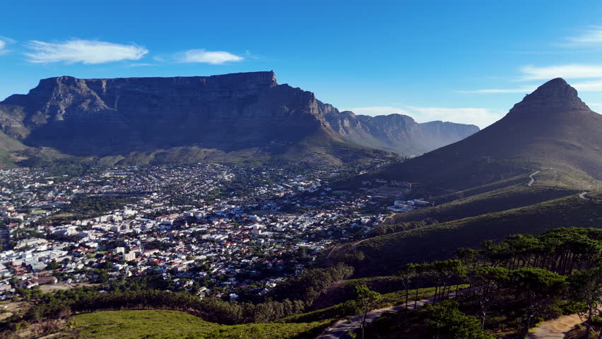 Cinematic aerial view of Table Mountain and Cape Town cityscape, showcasing rugged cliffs, urban sprawl, and South Africa’s iconic natural landmark under clear blue sky