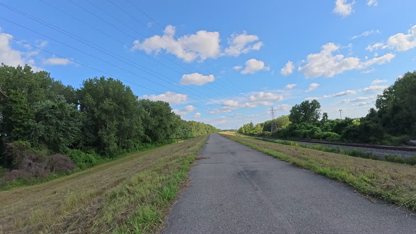 POV biking along the Riverfront Trail on a levee above the Mississippi River near St. Louis, Missouri. Scenic ride with wide river views, green embankments, and a peaceful trail on top of levee.