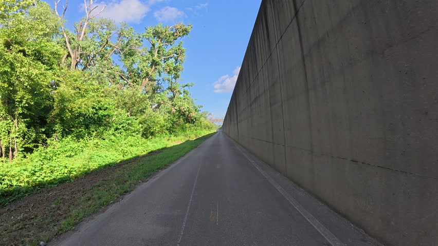 POV cycling on the Riverfront Trail alongside a massive concrete floodwall near the Mississippi River above St. Louis, Missouri - flood protection wall, and unique riverside infrastructure.