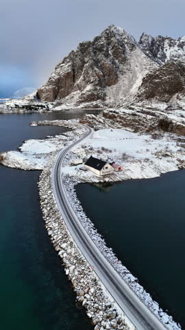 Cinematic aerial view of snowy coastal village and bridge in Lofoten, Norway, scenic arctic seascape with islands, winter shoreline, and dramatic Nordic landscape