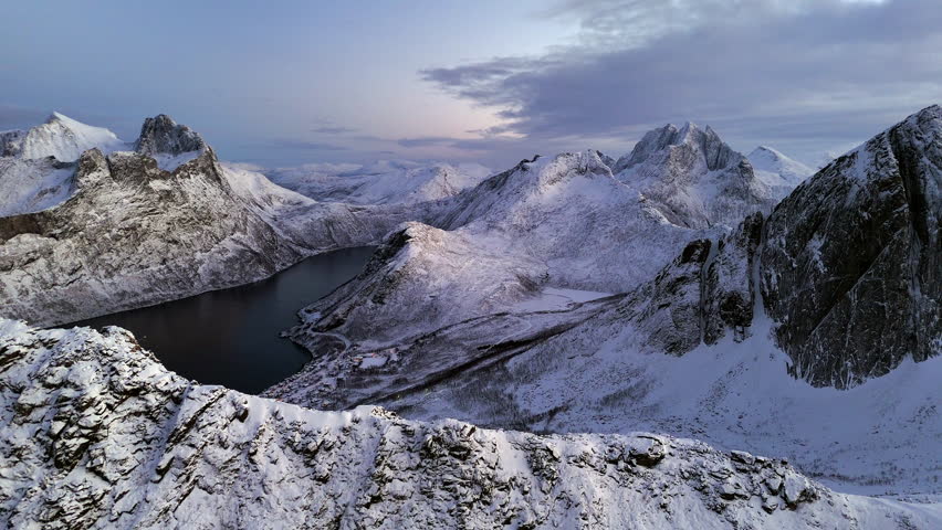 Cinematic aerial view of Segla peak on Senja Island, Norway, steep snow-covered cliffs above icy fjord, dramatic arctic landscape with rugged mountains and winter wilderness