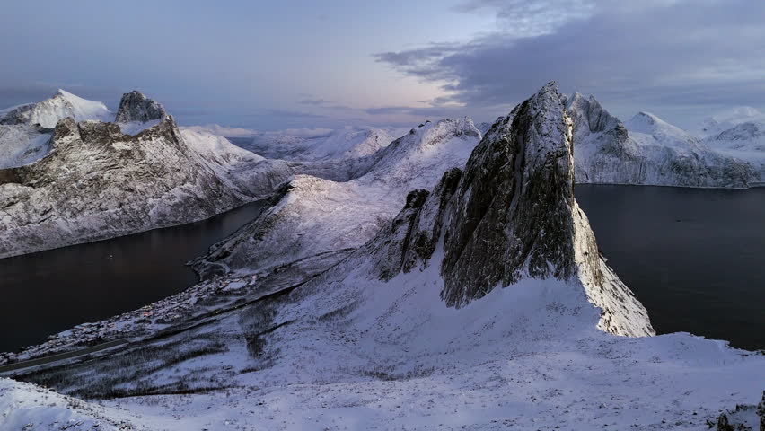 Cinematic aerial view of Segla peak on Senja Island, Norway, steep snow-covered cliffs above icy fjord, dramatic arctic landscape with rugged mountains and winter wilderness